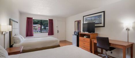 A hotel room with two beds, a desk, a chair, a TV, a dresser, and a window with curtains.