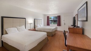 A hotel room with two beds, a wooden desk, a TV, and a window with curtains.