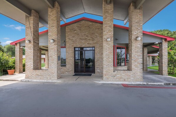 A building with a brick facade, a glass entrance, and a red roof. - Americas Best Value Inn Lockhart (Lockhart)