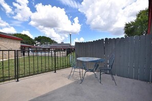 A patio with a metal table and chairs, a wooden fence, and a building in the background. - Americas Best Value Inn Lockhart (Lockhart)