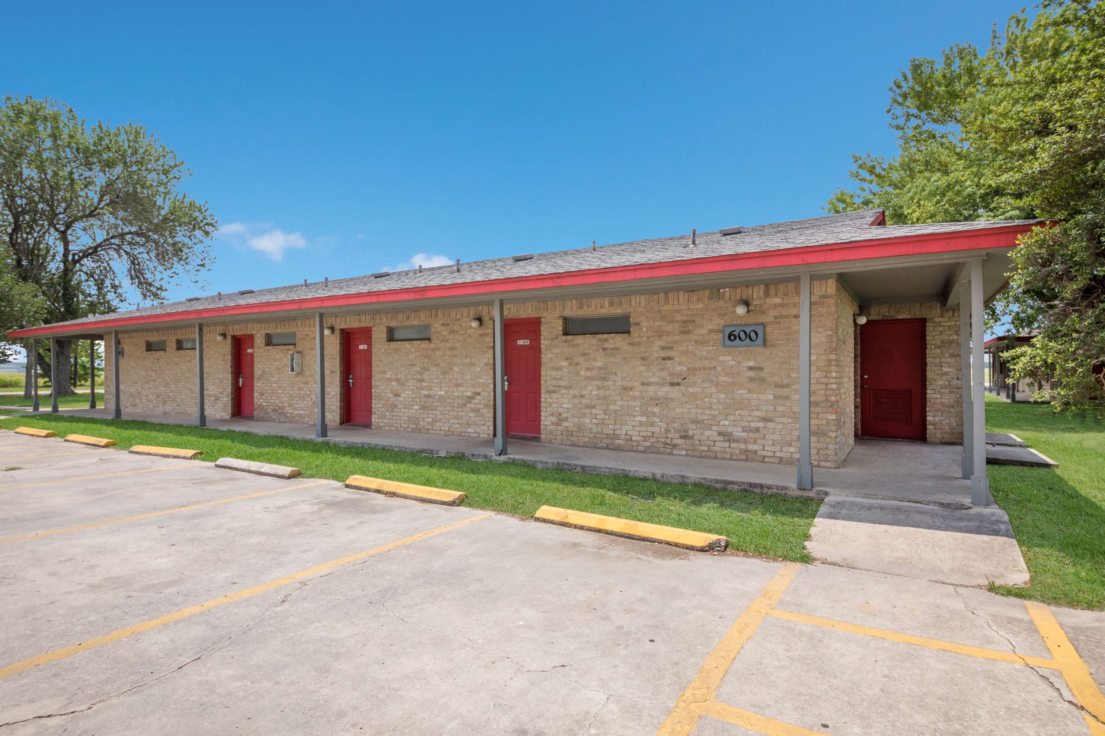 A motel with a brick facade, red doors, and a parking lot with yellow lines.
