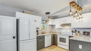 A modern kitchen with white cabinets, a stainless steel refrigerator, a built-in oven, and a granite countertop. - Quaint Cottage by the Bay - Boat Launch 1 Street Over (Elberta)
