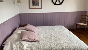 Un dormitorio con cama, una silla, una rueda de barco montada en la pared y un cuadro enmarcado.