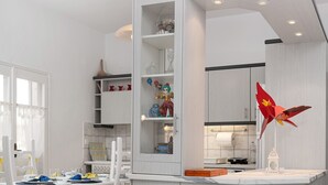 Uma cozinha moderna com esquema de cores branco e cinza, uma área de jantar com mesa branca e cadeiras vermelhas, e uma peça decorativa vermelha e singular no balcão.