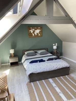 Um quarto com teto inclinado, painel de parede com mapa mundi, cama com roupa de cama estampada, abajur e uma pequena mesa de cabeceira de madeira.