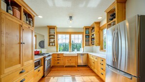 A kitchen with wooden cabinets, a stainless steel refrigerator, and a window providing a view of the outdoors. - Rancho Relax Inn  (CARLTON)