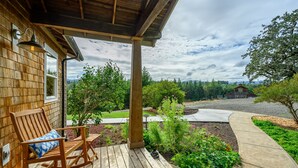 A wooden deck with a rocking chair, a potted plant, and a view of a rural landscape with a barn. - Rancho Relax Inn  (CARLTON)