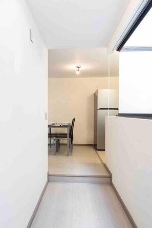 Un couloir étroit mène à une petite cuisine équipée d’un réfrigérateur et d’une table à manger avec des chaises.