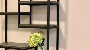 Una estantería metálica negra con un florero con flores verdes en una de sus repisas.