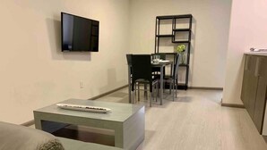 Una sala de estar moderna con un televisor de pantalla plana, un comedor con mesa y sillas, y una cocina con armarios.