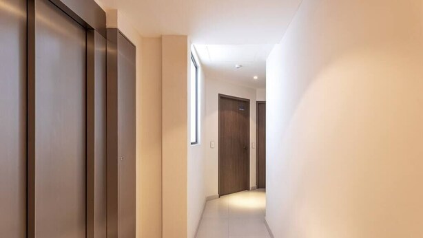 Un couloir doté d’un ascenseur moderne et d’une porte au bout.