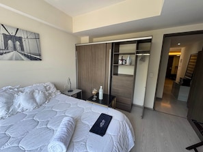 Une chambre d’hôtel avec un grand lit, une armoire, un bureau avec une lampe et un tableau au mur.