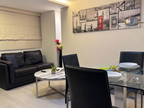 Ein modernes Wohnzimmer mit einem Glastisch, einer schwarzen Ledersofa und einem Stadtbild an der Wand.