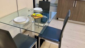 Une cuisine moderne avec une table à manger en verre, des chaises et un plan de travail blanc.
