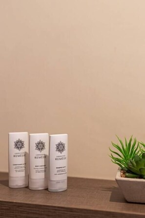 Three Remède bottles on a wooden shelf with a potted plant beside them.