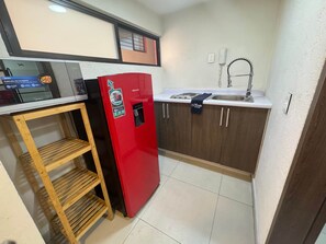 A compact kitchen with a red refrigerator, a wooden shelf unit, and a sink with a faucet.