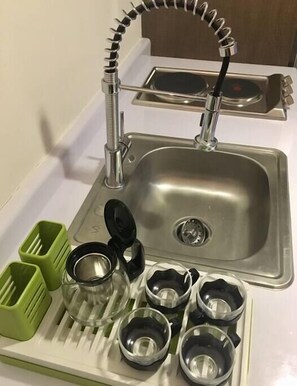 A kitchen sink with a modern faucet, a stainless steel basin, and a dish drying rack with green and clear containers.