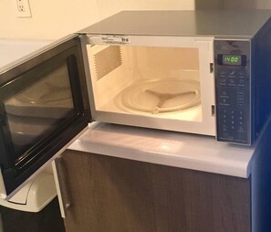 A microwave oven with a digital display, placed on a wooden cabinet.