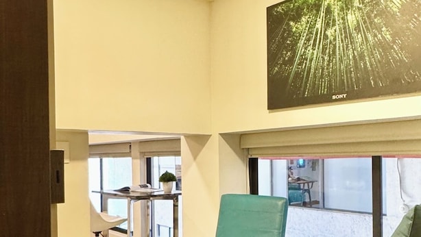 A modern living room with a teal armchair, a black sofa, and a small table with magazines. A large window allows natural light and views of the outside. - Reliable Double-Height Stay. Great CDMX Location (Mexico City)