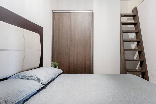 A bedroom with a bed, a wooden wardrobe, and a wooden ladder against the wall.
