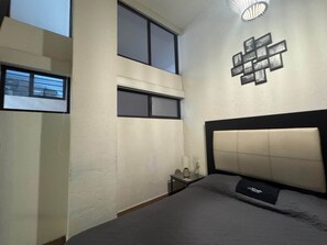 Een slaapkamer met een bed, nachtkastje, wandlamp en een raam.