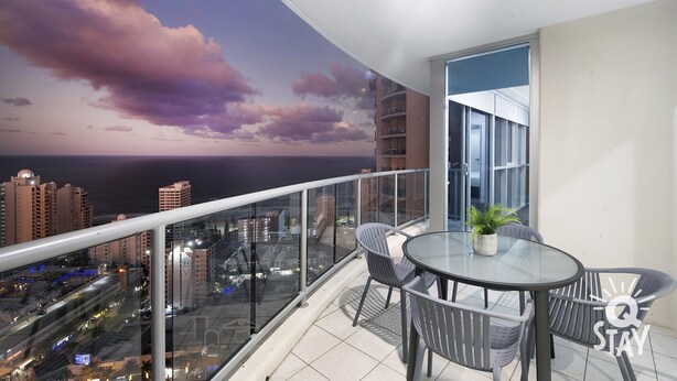 A balcony with a glass table and chairs, a potted plant, and a cityscape view. - 3 Bed Executive Sub Penthouse with Ocean Views (Surfers Paradise)