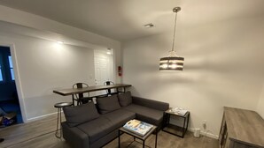 A modern living room with a sectional sofa, a coffee table, and a dining area with a long table and chairs. - Charming 4bedroom 2nd Floor Beach House - 1.5 blocks to the beach (Long Branch)