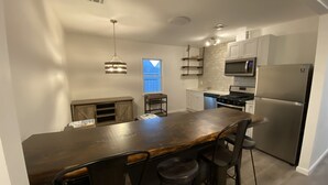 A modern kitchen with a central island, bar stools, stainless steel appliances, and a hanging light fixture. - Charming 4bedroom 2nd Floor Beach House - 1.5 blocks to the beach (Long Branch)