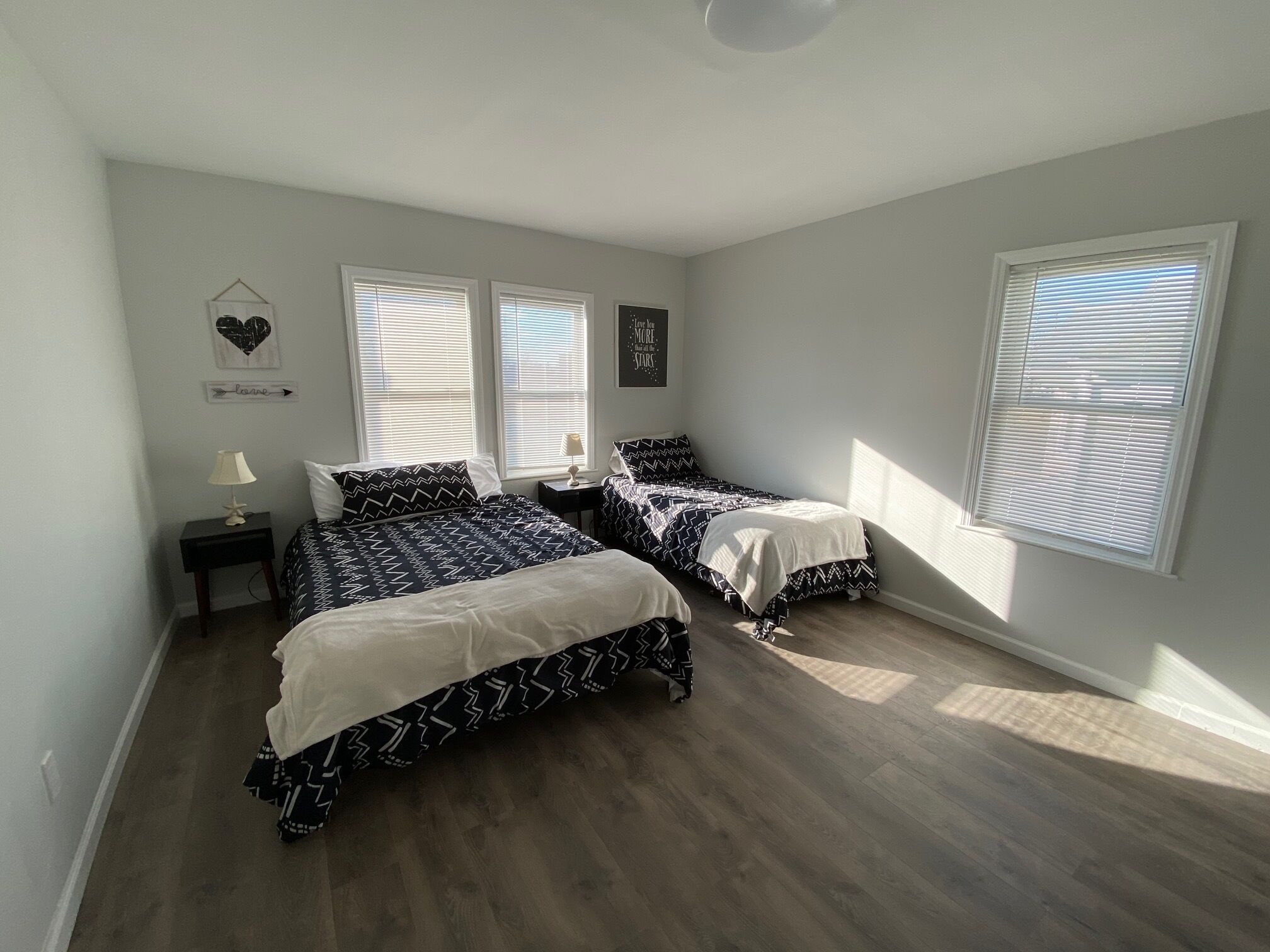 Une chambre avec deux lits, une table de chevet, une lampe et un mur décoré d’un motif en forme de cœur et d’une inscription.