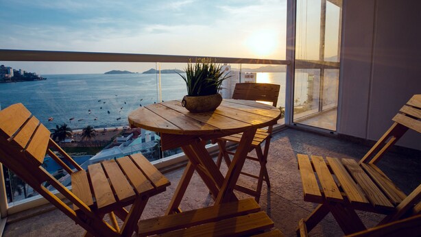 Une table et des chaises en bois sur un balcon offrant une vue sur la mer et les îles lointaines.