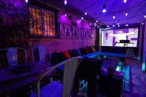 A dimly lit room with a blue-lit seating area, a projector screen, and a table with a remote control.