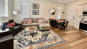 A living room with a sofa, coffee table, and a dining area with chairs and a table. There is a ceiling fan, a lamp, and a kitchen area with cabinets and a microwave. - New - Lookout Views 2 Br/2BA Sleeps 8 next to OddStory Brewery! Pet friendly! (Chattanooga)
