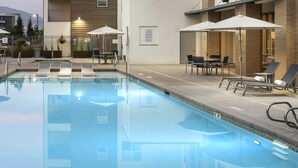 A swimming pool with lounge chairs and umbrellas, surrounded by a building with multiple floors and windows. - Experience South Valley charm, just a 9-min drive to Thanksgiving Point (Draper)