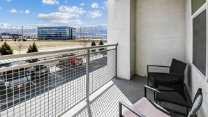 A balcony with a view of a parking lot, a building with signage, and mountains in the background. - Experience South Valley charm, just a 9-min drive to Thanksgiving Point (Draper)