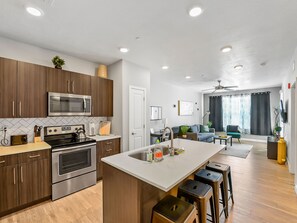 A modern kitchen with stainless steel appliances, wooden cabinets, and a central island with stools. - Experience South Valley charm, just a 9-min drive to Thanksgiving Point (Draper)
