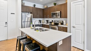 A modern kitchen with stainless steel appliances, wooden cabinets, and a white countertop. - Experience South Valley charm, just a 9-min drive to Thanksgiving Point (Draper)