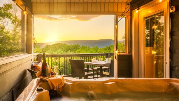 Un bain à remous sur un balcon avec vue sur une forêt et des montagnes.