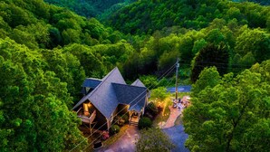 Une cabane dotée d’un toit en pente, entourée d’une forêt dense, et disposant d’un espace extérieur aménagé pour s’asseoir.