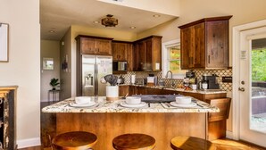 Une cuisine moderne avec des meubles en bois, un réfrigérateur en acier inoxydable, un four encastré et un grand îlot central doté de tabourets de bar.