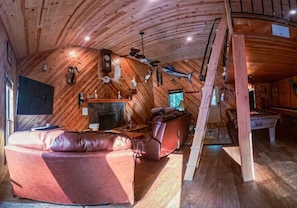 Ein gemütliches Blockhaus mit Holzwänden, Kamin, Ledersitzmöbeln und einem Billardtisch.