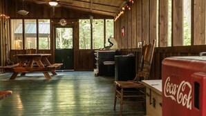 L’intérieur d’un chalet rustique, avec des murs en bois, un plancher en bois, une table, des chaises, un bureau, un fauteuil, un extincteur et un réfrigérateur pour les boissons, notamment du Coca-Cola.