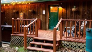 Une cabane en bois avec un porche, une porte verte et des sièges à l’extérieur.