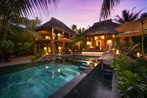 A resort with a swimming pool, thatched-roof structures, and outdoor seating areas.