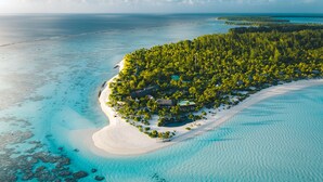 Vista aérea de una isla tropical con una playa de arena blanca, aguas turquesas cristalinas y densa vegetación verde.