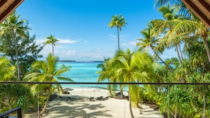 Una terraza de madera con vista a una playa y palmeras.