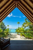 A wooden deck with a view of a beach and palm trees.