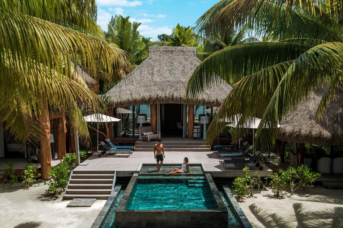 A pool area with a thatched-roof structure, lounge chairs, and palm trees.