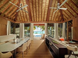 A spacious dining area with a view of the ocean, wooden ceiling beams, and ceiling fans.