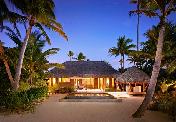 Un resort frente a la playa con construcciones de techo de paja, piscina y palmeras.