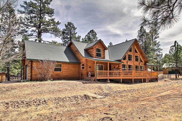 A large log cabin with a porch and multiple windows, surrounded by trees. - Family Game Room: Spacious Overgaard Cabin (Overgaard)